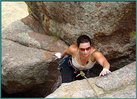 N. Edwards emerging into the light from the darkness near the top of Hideaway Chimney.  The Turtle Rock Trail can be seen in the upper left background.