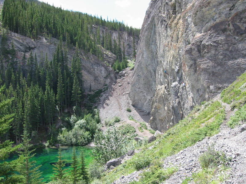 <br>
Grassi is a great place to escape summer heat waves. The trail from the dam down to Grassi Lakes is in the gully, center. The belay platforms for Meathooks can be seen in the shady alcove right of the lake.          <br>
<br>
One problem unique to Grassi is the occasional rockfall.  The Spray Lakes road is just above the meathooks wall and non-climbers will sometimes toss rocks.  