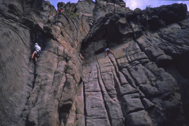 Tony Bubb approaches the pumpy roof of 'Pass/Fail Option (5.11)' from the top of 'The Final Exam (5.11),' at right. Unknown clmbers on Curving Crack, at left. Photo at Castle Rock in Boulder Canyon by Dianne Conelly, in 2001.