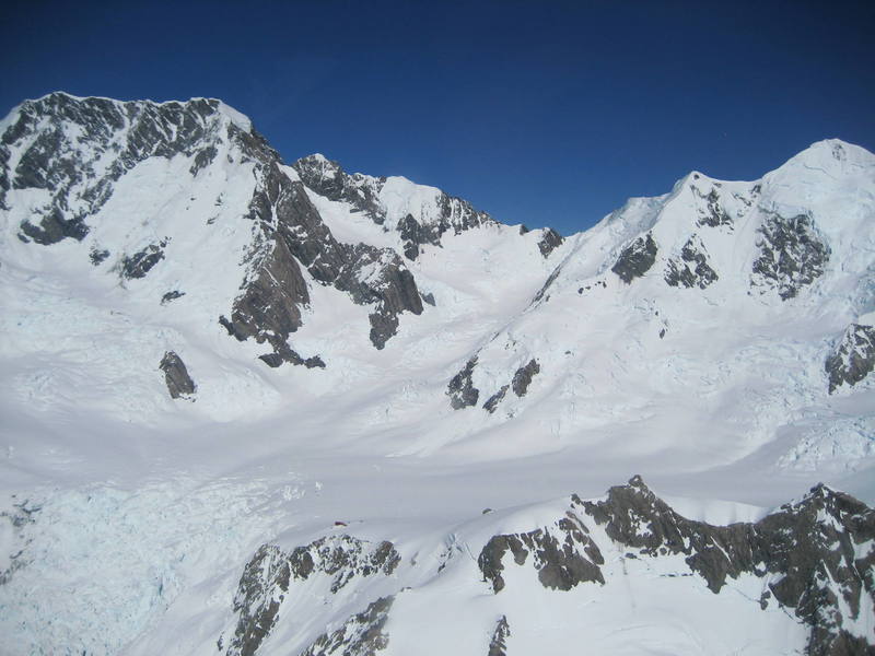 This is the grand plateau below Mt. Tasman and Mt. Cook.  In the bottom left/center, atop the rocky outcrop, sits an alpine hut with a red roof.  Every year, hundreds of climbers use it as basecamp for alpine ascents of Mt. Cook (left) and Mt. Tasman (right). 