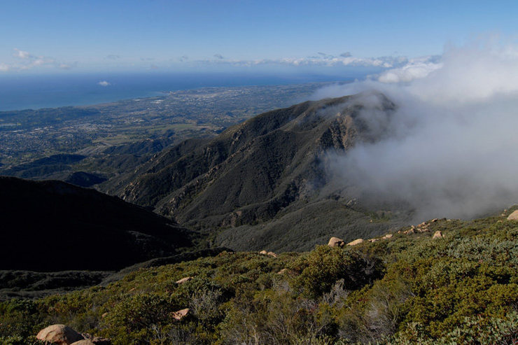 The view west toward UCSB from La Cumbre Peak, as clouds spill over Camno Cielo from the Santa Ynez Valley.