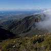 The view west toward UCSB from La Cumbre Peak, as clouds spill over Camno Cielo from the Santa Ynez Valley.