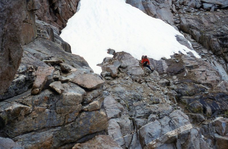 A view on the left of the irregular and sloping ledge, referred to as the Catwalk, which unlocked the key for the first ascent of North Palisade. D. Selby is sitting below the snowfield on the edge of the Southwest Chute leading up to the U-Notch.  Photo taken 21 Aug 95.