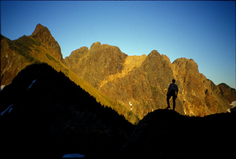 Don Serl silhouetted in front of the Settler. The traverse from south to north climbs the skyline from right to left to the second-from-left summit then descends gullies below that summit. The apparent highest summit at far left is actually a gendarme on the NW ridge.