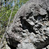 This climbs up the back side of the Amateur boulder, starting on 2 good holds above the hole between the boulders. Climbs slightly left & then up the slab