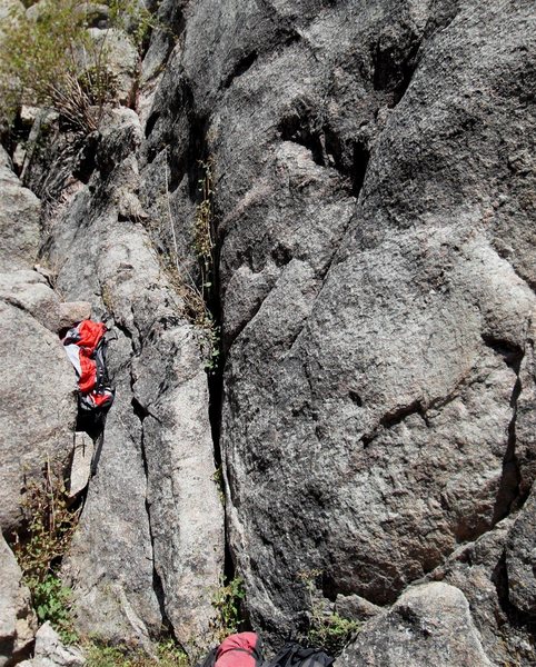 The regular start follows the easy crack to the right of the red backpack.  It angles up and left about 15 feet to a small ledge, then you walk right along the ledge until you get to the crack for pitch one.  (See the other photo of the direct 5.9+ start).