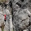 The regular start follows the easy crack to the right of the red backpack.  It angles up and left about 15 feet to a small ledge, then you walk right along the ledge until you get to the crack for pitch one.  (See the other photo of the direct 5.9+ start).