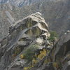 Zoomed view from the summit of the Organ Needle of me considering the mantle up to the unprotected lichen covered slab below the summit block.  Ultimately I traversed around to the right and climbed a short awkward corner. (photo by Asher)