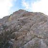 Looking up at the NE face from the col.  Belay from here, or the brushy alcove above, climb left of the roof where the rappel can be seen above. 