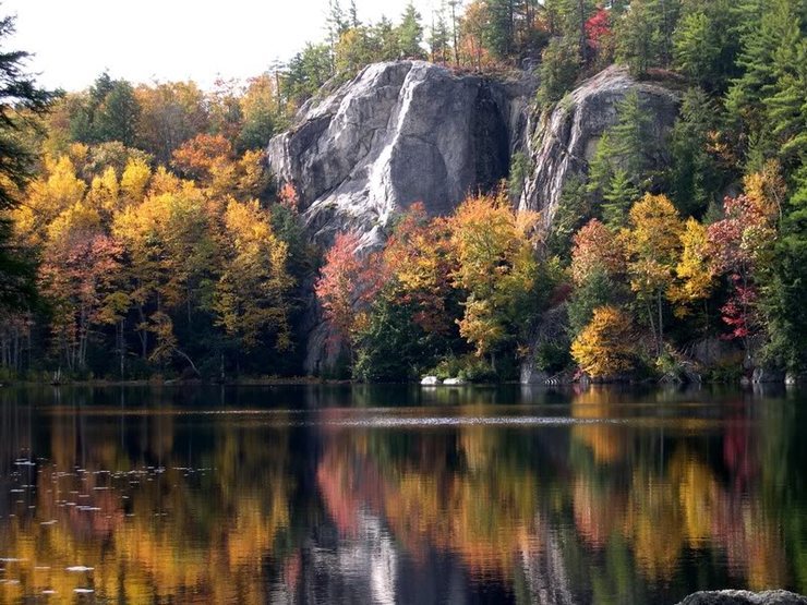 Stonehouse Pond in October. On the far left you can see the top of the routes Moe Howard Died for Our Sins and Geezer Pleaser. The sun/shade line ridge is The Nose. Slab with the pine tree growing out of it is Down by Law. The face to the far right is the Luna Wall.