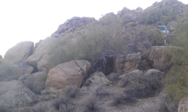 The Den Boulder is to the left of the guy and behind The mesquite tree you can barely see the top of Den Boulder. If your walking north this will be to your left. 