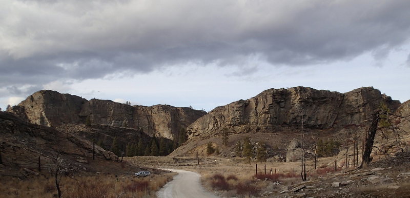 County road with a vehicle at the south parking pullout, and the cliffs to the North.