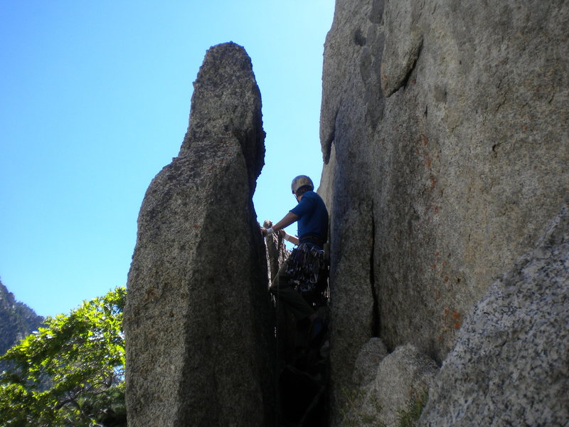 Go left across the brush-laden ledge and squeeze behind this flake. It leads right to the start of the crack