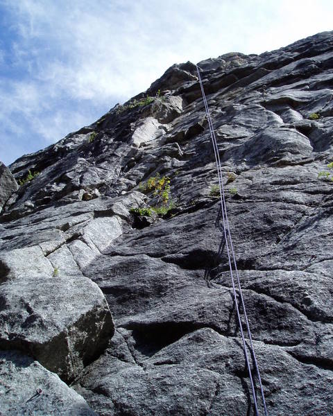 This photo shows all of pitches 1 and 2. P1 climbs the series of right facing corners and then moves left at the bottom of the last corner before the roof to belay near the green vegetation. P2 climbs up then right and back left through the roof where the rope is hanging from the skyline.