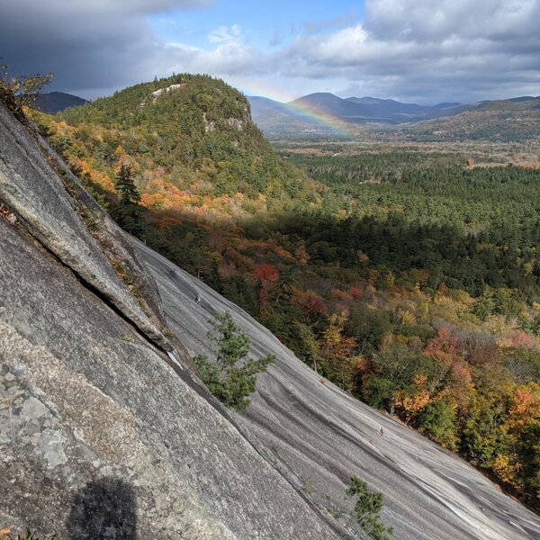 Looking across Whitehorse slabs from Sea of Holes at a rainbow behind Cathedral Ledge.