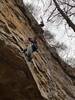 Looking up from the ground past the belayer at the belay station to the climber at the top of the route